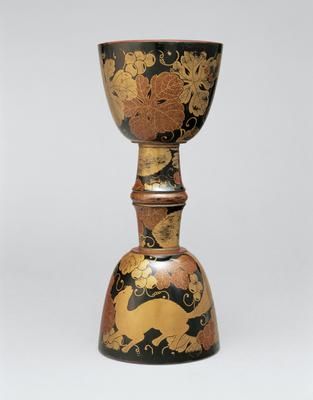 drum core in shape of two adjoined chalices; black lacquer with gold flecked grape vines, leaves, and squirrels