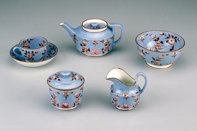 light blue with brown stems, leaves and rims; flowers have been hand painted; crafted in light weight pottery; teapot cover is recessed with a steam hole in the center of the finial; cream pitcher has a wide lip; sugar bowl fits over the base; waste bowl is large