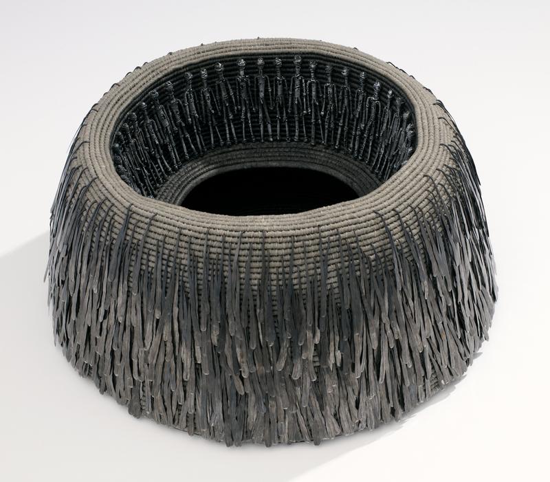 grey bowl form made of rings of looped fibers; darker grey interior and bottom; dark iron wire standing male figures around inner rim; exterior decorated with drip-shaped iron drops hooked between woven fibers