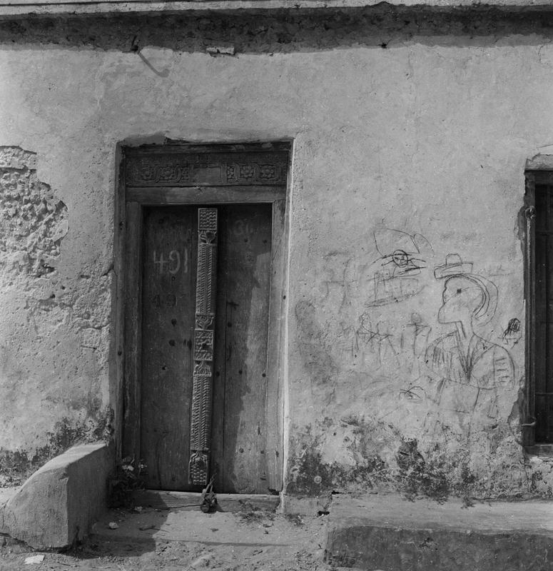 Black and white image of a doorway with 491 on it; graffiti on the wall to the right